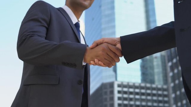 Low angle view of two male business partners shaking hands with each other outside of office building