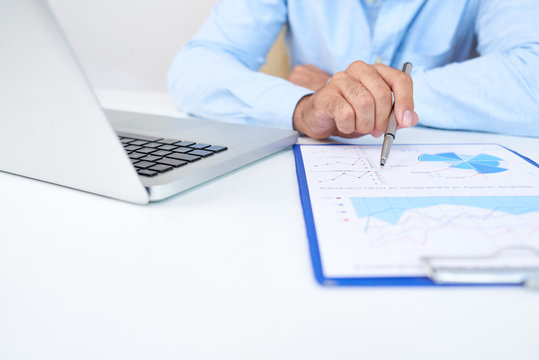 Entrepreneur sitting at office table and checking document with financial chart when working on laptop