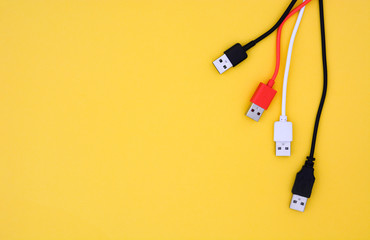 top view black, white and red color USB cables on yellow background with copy space, flat lay