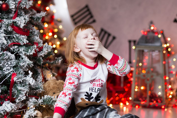 Portrait of yawning girl wearing pajama on beautiful Christmas background. Celebrating Xmas indoors.