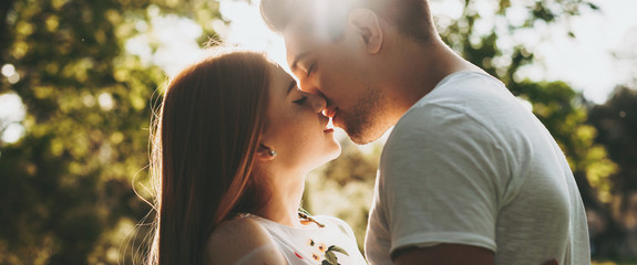 Side view portrait of a amazing caucasian couple kissing against golden hour light embracing while...