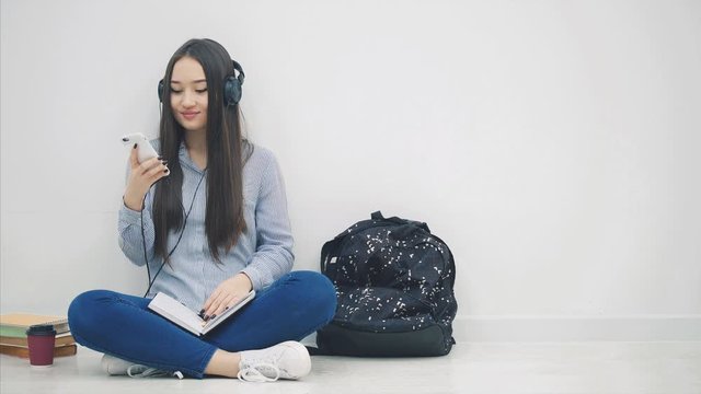 Inspired young asian girl sitting on the floor, doing homework, listening to music, switching over songs, dancing.