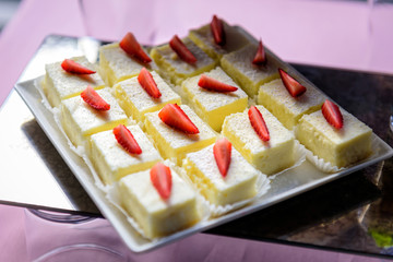 Portion biscuit cakes with buttercream decorated with fresh strawberries close-up. Sweets at festive banquet.