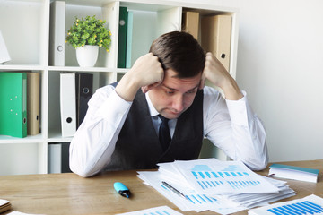 Sad businessman with business report and stack of papers in the office.