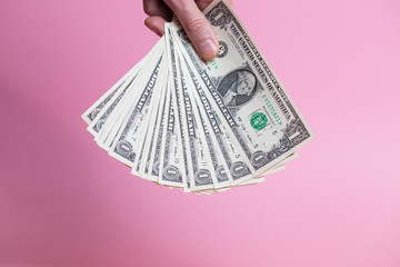 A bundle of dollar bills in a male hand on a pink background.