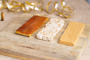 Three type of  Spanish turron, hard almond, soft almond and burnt egg yolk nougat on wooden cut board with Christmas decoration