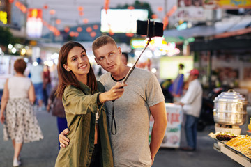 Hugging young Caucasian couple taking selfie at Vietnamese street market