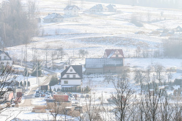 Fototapeta na wymiar PIENIAZKOWICE, POLAND - DECEMBER 06, 2019: View of the village houses situated on the hills on a foggy winter morning.