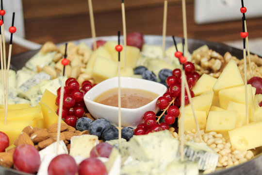 Plate with cheese, berries and nuts at the party. Fresh snacks with wooden stick and sauce plate. Healthy holiday treat. Food photography. Red currant, blueberry, grapes, almond, walnut, pine nuts