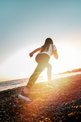 The concept of sport and running. A woman in sportswear at a low start for a run. Rear and bottom view. In the background, the sky and sea. Copy space. Sunlight. Diagonal horizon line