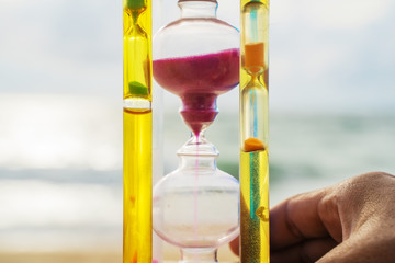 The hourglass passing time on the beach The hourglass in front of the bright blue sky with white...