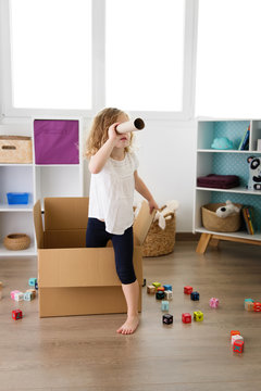 Young girl looking through cardboard tube while standing in box