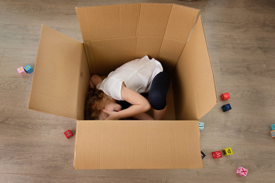 Playful young child hiding in cardboard box