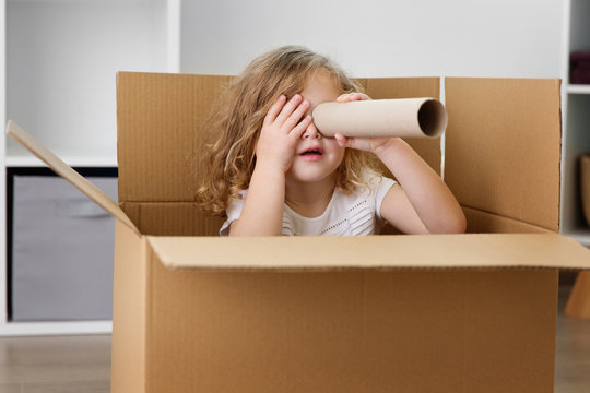 Young girl looking through cardboard tube while sitting in box