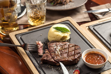 Grilled Ribeye Steak with knife and fork and mashed potato on stone board on wooden table at restaurant