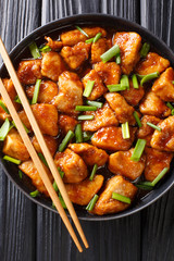 Asian food stir-frying chicken in sweet sauce with green onion close-up in a plate. Vertical top view