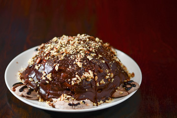 Traditional Russian anthill cake with chocolate and nuts on a black wooden background.