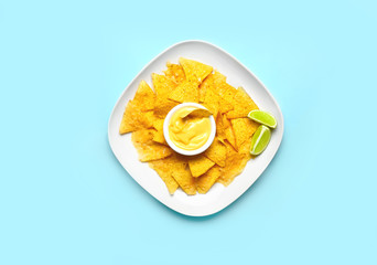 Plate with tasty nachos and sauce on color background