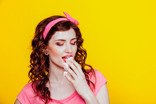 girl in pink dress pinup-style eats cake with cream
