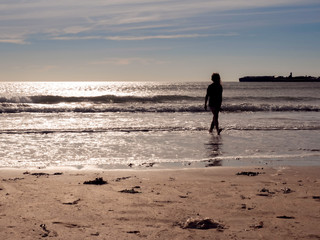 Naklejka premium Silhouette of a teenager girl walking in water at sunset. Concept childhood, outdoor activity, fun, youth.