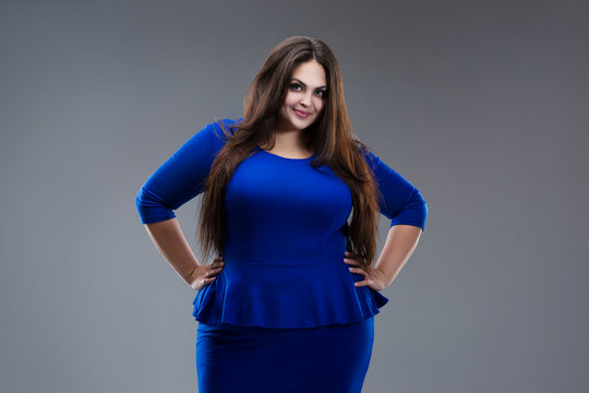 Happy plus size model in blue dress, fat woman with long hair on gray background, body positive concept