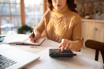 Dark-haired young woman in sweater making calculations
