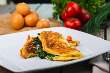 Traditional omelet with vegetables, spinach, tomatoes and herbs on a wooden table in a restaurant.
