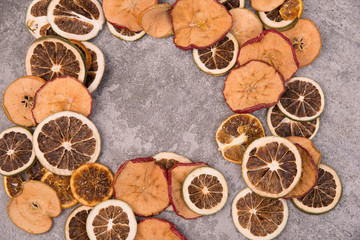 Slices of dry lemon, oranges and apples on a grey structured background