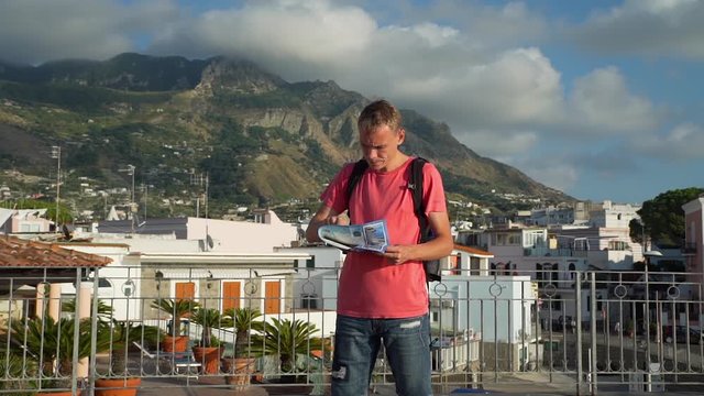 Tourist Man Trying to Determine Location on the Map. He is Exploring Italian City on Ischia Island in Italy at Sunset. Concept of Holidays, Vacations and Travel in Europe