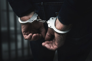 Fototapeta arrested man with cuffed hands behind prison bars obraz
