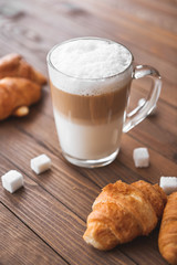 Glass cup of tasty latte with croissants on wooden table
