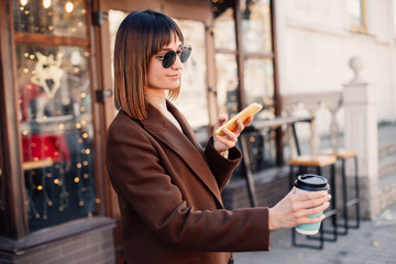 Woman drinking coffee and using phone on street.
