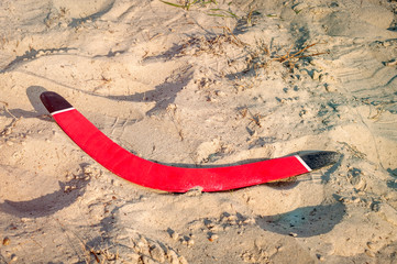 Red wooden boomerang lies in the sand