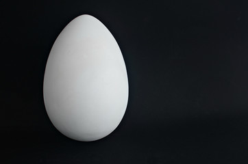 White plaster egg on a black background. Abstract geometric shape. Copy space.