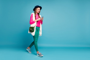 Fototapeta na wymiar Full length body size view of her she nice attractive lovely cheerful cheery girl walking spending free time using gadget isolated on bright vivid shine vibrant green blue turquoise color background