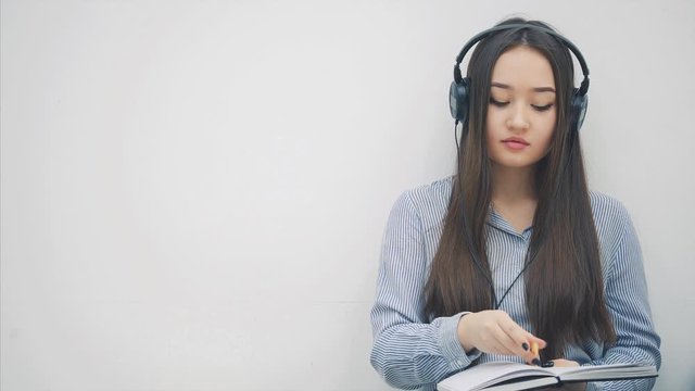 Inspired young asian girl sitting on the floor, writing, listening to music, then she got message and take her phone to answer.