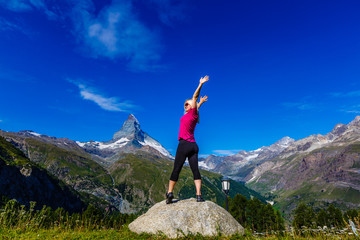 Young girl holds hands up against the sky and mountain