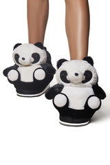 Close-up shot of female legs in funny black and white plush house slippers made in the form of pretty panda. The photo is made on the white background.
