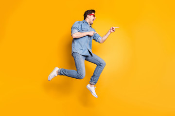 Fototapeta na wymiar Full length body size view of nice attractive funky crazy cheerful cheery guy jumping pointing aside advert hot tour trip isolated over bright vivid shine vibrant yellow color background