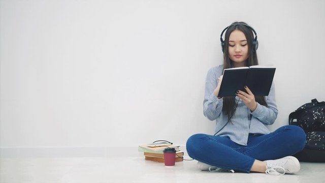 Inspired young asian girl sitting on the floor, writing, listening to music, then she got message and take her phone to answer.