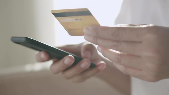 Side view. Hand of young woman are buying online with a credit card while sitting on the sofa. Women are using smartphone and doing online transactions.