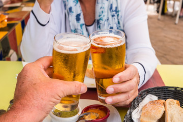 Two people enjoy a glass of cold beer with some appetizers. Refreshing and gold colored beer. Bar table