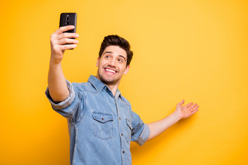 Photo of positive stylish man smiling toothily indicating empty space with his arms hand inviting...