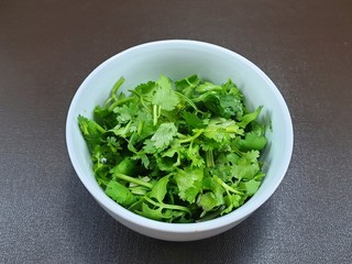 Top view of fresh coriander leaf in white bowl isolated on wooden background for sale in the supermarket, for making cooking, healthy food concept