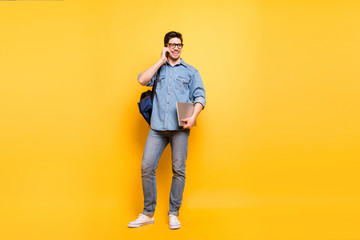 Fototapeta premium Full length body size photo of cheerful positive toothy beaming man with laptop in hand speaking by phone in white sneakers isolated vibrant color background