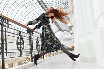 Conceptual posing. Caucasian model with long red hair in a black dress with a floral print and...