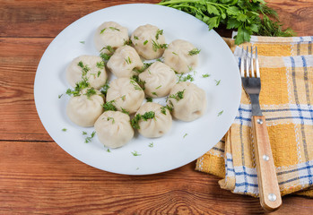 Boiled khinkali with chopped dill on dish, fork on napkin