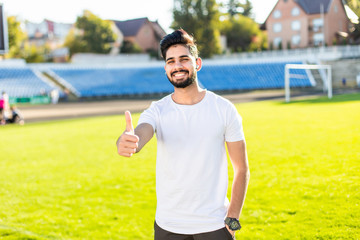 Handsome indian man or guy with muscular body showing thumb up sunny outdoor in blue sportswear at stadium. fitness and healthy lifestyle concept
