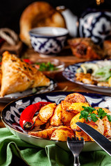 The concept of Uzbek cuisine. Different oriental dishes on the table in national Uzbek plates. Rustic fried potatoes. background image. copy space