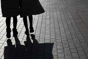 Two girls in coats walking down the street, black silhouettes and shadows on pavement. Female...